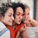 Three women enjoying a playful moment with heart-shaped glasses, symbolizing friendship and fun.