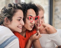 Three women enjoying a playful moment with heart-shaped glasses, symbolizing friendship and fun.